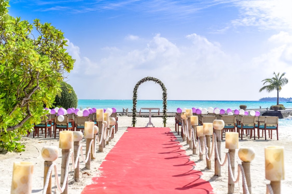 Premium outdoor destination wedding setup on a sandy beach with a red carpet and flower arch